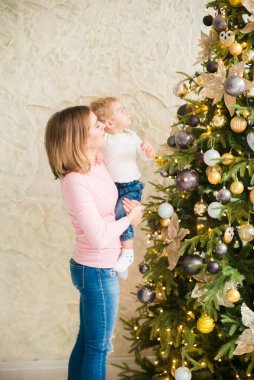 Sarışın, sevimli küçük çocuk, Noel ağacının yanında süslenmiş parlak bir odada annesiyle oynuyor. Mutlu bir çocukluk. Noel havası
