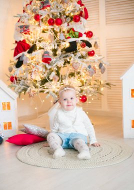 Sarı saçlı şirin küçük kız, Noel ağacının yanındaki parlak bir odada Noel çelenkleriyle oynuyor. Mutlu bir çocukluk. Noel havası