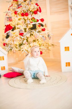 Sarı saçlı şirin küçük kız, Noel ağacının yanındaki parlak bir odada Noel çelenkleriyle oynuyor. Mutlu bir çocukluk. Noel havası
