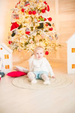 Sarı saçlı şirin küçük kız, Noel ağacının yanındaki parlak bir odada Noel çelenkleriyle oynuyor. Mutlu bir çocukluk. Noel havası