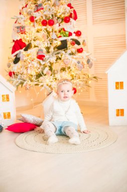 Sarı saçlı şirin küçük kız, Noel ağacının yanındaki parlak bir odada Noel çelenkleriyle oynuyor. Mutlu bir çocukluk. Noel havası
