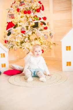 Sarı saçlı şirin küçük kız, Noel ağacının yanındaki parlak bir odada Noel çelenkleriyle oynuyor. Mutlu bir çocukluk. Noel havası