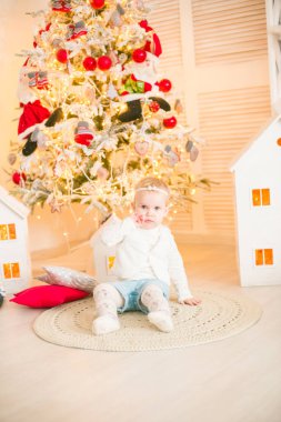 Sarı saçlı şirin küçük kız, Noel ağacının yanındaki parlak bir odada Noel çelenkleriyle oynuyor. Mutlu bir çocukluk. Noel havası
