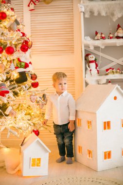 Sarışın şirin çocuk, Noel ağacının yanında süslenmiş parlak bir odada oyuncaklarla oynuyor. Mutlu bir çocukluk. Noel havası