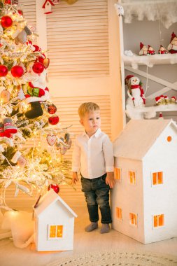 Sarışın şirin çocuk, Noel ağacının yanında süslenmiş parlak bir odada oyuncaklarla oynuyor. Mutlu bir çocukluk. Noel havası