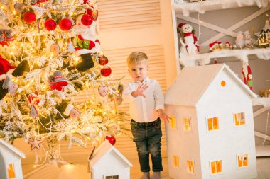 Sarışın şirin çocuk, Noel ağacının yanında süslenmiş parlak bir odada oyuncaklarla oynuyor. Mutlu bir çocukluk. Noel havası