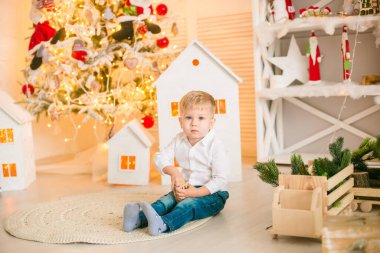 Sarışın şirin çocuk, Noel ağacının yanında süslenmiş parlak bir odada oyuncaklarla oynuyor. Mutlu bir çocukluk. Noel havası