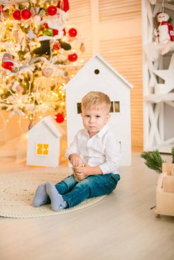 Sarışın şirin çocuk, Noel ağacının yanında süslenmiş parlak bir odada oyuncaklarla oynuyor. Mutlu bir çocukluk. Noel havası