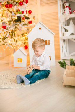 Sarışın şirin çocuk, Noel ağacının yanında süslenmiş parlak bir odada oyuncaklarla oynuyor. Mutlu bir çocukluk. Noel havası