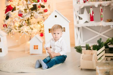 Sarışın şirin çocuk, Noel ağacının yanında süslenmiş parlak bir odada oyuncaklarla oynuyor. Mutlu bir çocukluk. Noel havası