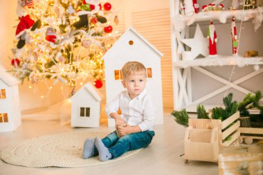 Sarışın şirin çocuk, Noel ağacının yanında süslenmiş parlak bir odada oyuncaklarla oynuyor. Mutlu bir çocukluk. Noel havası