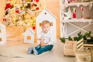 Sarışın şirin çocuk, Noel ağacının yanında süslenmiş parlak bir odada oyuncaklarla oynuyor. Mutlu bir çocukluk. Noel havası