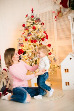 Sarışın, sevimli küçük çocuk, Noel ağacının yanında süslenmiş parlak bir odada annesiyle oynuyor. Mutlu bir çocukluk. Noel havası