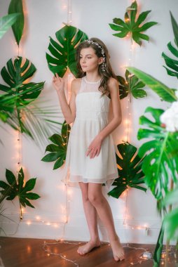 Tropik yeşillikler, beyaz orkideler, güller ve zambaklar arasında romantik beyaz elbiseli çekici bir genç kız. Güzellik ve moda