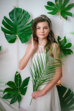 Tropik yeşillikler, beyaz orkideler, güller ve zambaklar arasında romantik beyaz elbiseli çekici bir genç kız. Güzellik ve moda