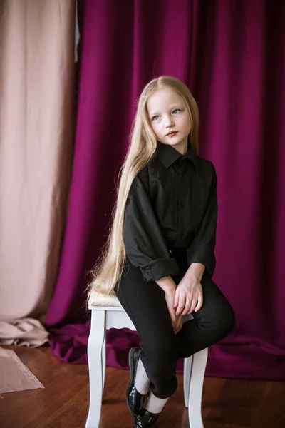在演播室里 一个漂亮的小女孩 一头长长的金发 穿着黑色衬衫 一条红色背景的牛仔裤 — 图库照片