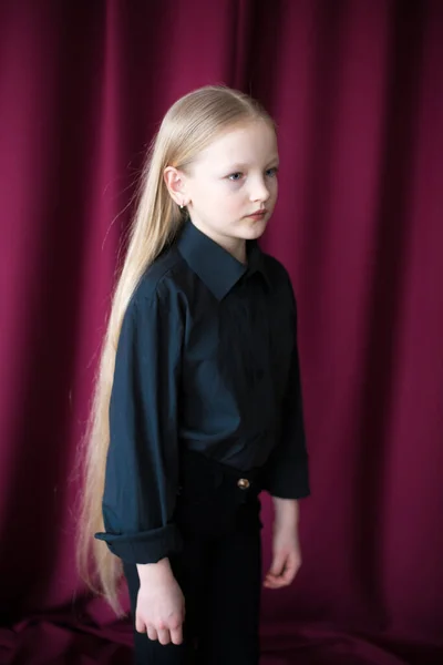 在演播室里 一个漂亮的小女孩 一头长长的金发 穿着黑色衬衫 一条红色背景的牛仔裤 — 图库照片