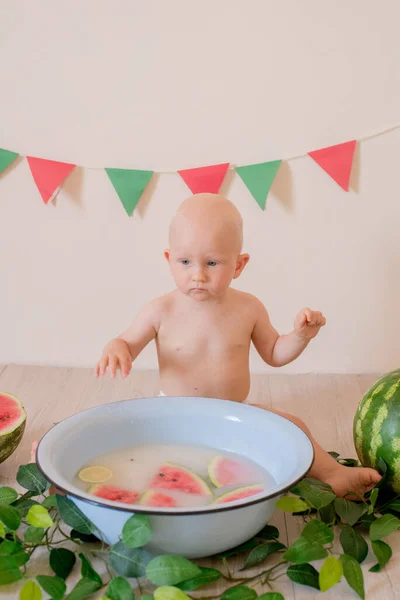 一个金发碧眼的可爱的小屁孩坐着 在一个明亮的背景上 在一盆水和西瓜中飞溅 儿童与水果 健康食品 — 图库照片
