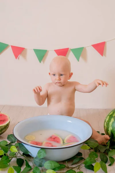一个金发碧眼的可爱的小屁孩坐着 在一个明亮的背景上 在一盆水和西瓜中飞溅 儿童与水果 健康食品 — 图库照片