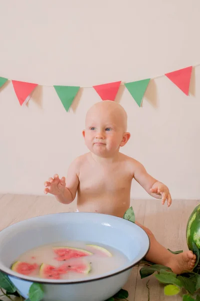 금발의 자그마하고 귀여운 아기가 배경에 수박이 물웅덩이에 물장구를 아이들 — 스톡 사진
