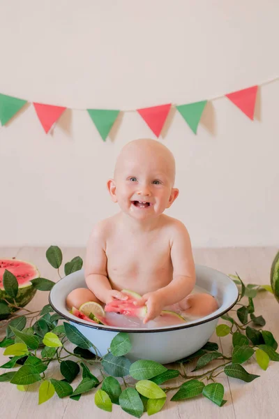 ブロンドの髪の小さなかわいい幼児が座って 明るい背景に水とスイカの流域に飛び散っています 子供と果物 健康食品 — ストック写真