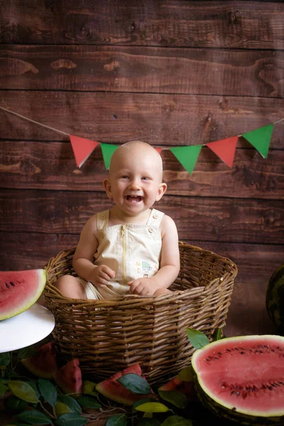 ブロンドの髪の小さなかわいい幼児は暗い木製の背景にスイカとバスケットに座っています 子供と果物 健康食品 — ストック写真