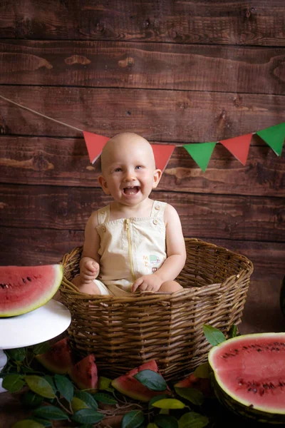 ブロンドの髪の小さなかわいい幼児は暗い木製の背景にスイカとバスケットに座っています 子供と果物 健康食品 — ストック写真