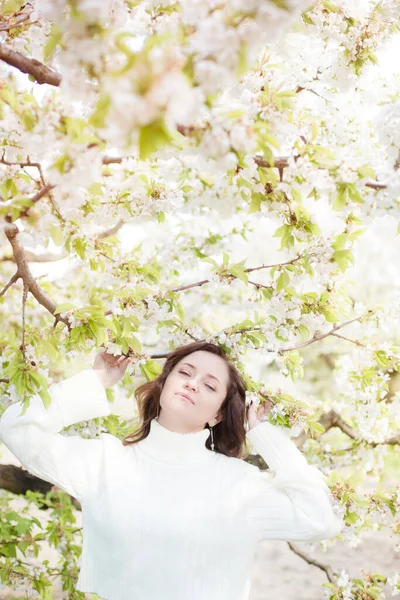 春に咲く桜の庭で白いニットセーターに茶色の髪のきれいな女性 春の自然 — ストック写真