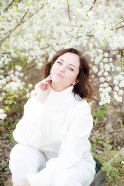美丽的女人 棕色的头发 白色的针织毛衣 春天在一个盛开的樱花花园里 春天的自然 — 图库照片