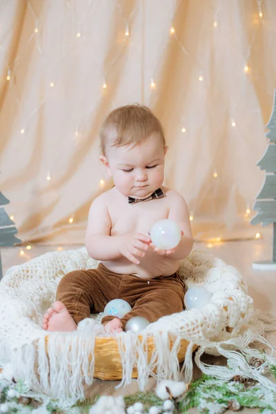 一个穿着吊袜带和领结的可爱的小男孩坐在一个用针头和圣诞球装饰的篮子里 节日气氛 圣诞快乐 — 图库照片
