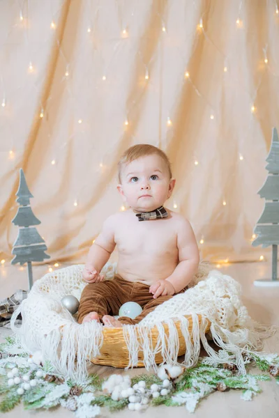 一个穿着吊袜带和领结的可爱的小男孩坐在一个用针头和圣诞球装饰的篮子里 节日气氛 圣诞快乐 — 图库照片