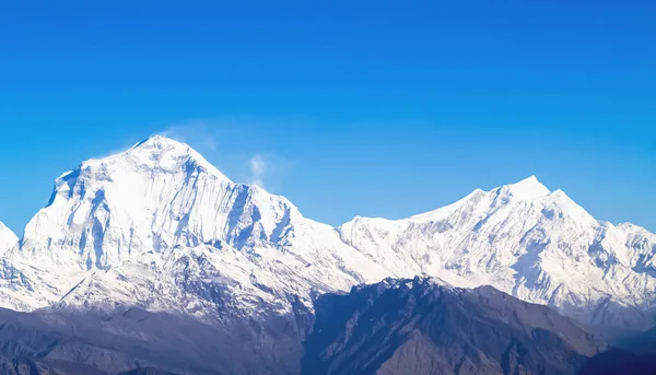 Paisaje de montaña. Majestuosos picos montañosos cubiertos de nieve contra un cielo azul brillante . — Foto de Stock