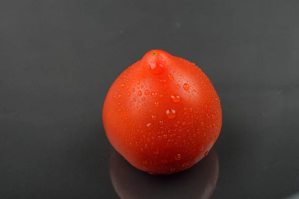 Single red tomato with drops isolated on black background. Juicy