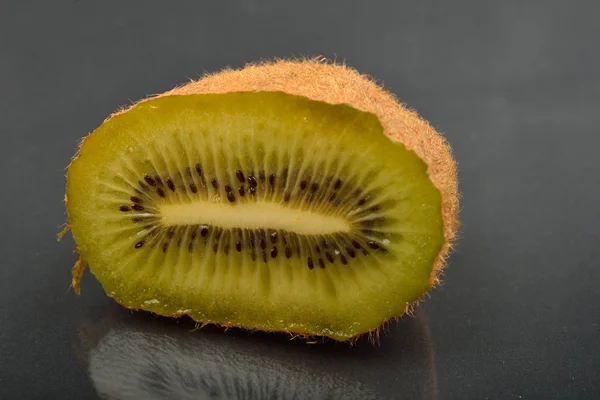 Menutup setengah kiwi dengan kulit berkerut pada backg refleksi gelap — Stok Foto