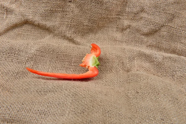 Piece of red pepper lying on on sackcloth background. Concept of — Stock Photo, Image