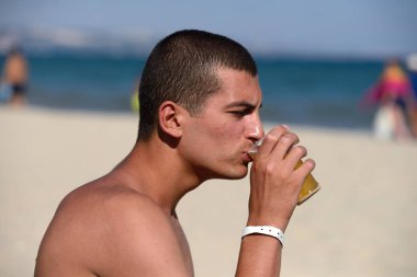 Young handsome sporty man drinking beer at the beach in summerti