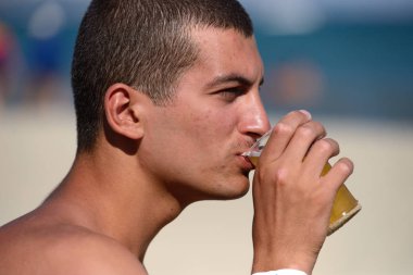 Young handsome sporty man drinking beer at the beach in summerti