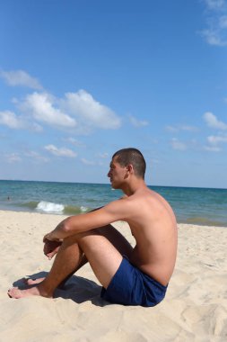 Young man with athletic body in blue shorts standing on the sand