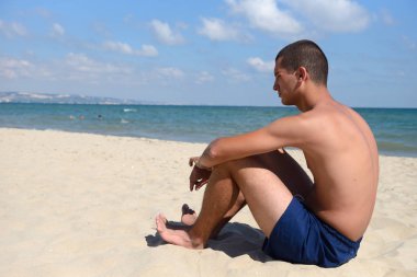 Young man with athletic body in blue shorts standing on the sand