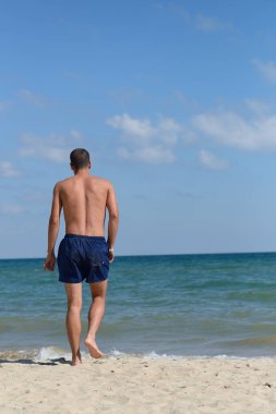Young man with athletic body in blue shorts is walking true the 