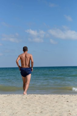 Young man with athletic body in blue shorts is walking true the 