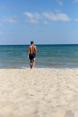 Young man with athletic body in blue shorts is walking true the 