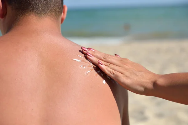 Main d'une femme appliquant de la crème solaire sur un dos masculin avec crème solaire — Photo