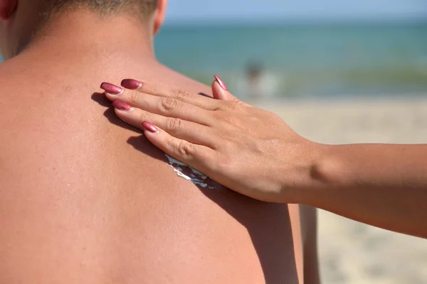 Hand of a woman applying sun cream on a male back with sunscreen — Stock Photo, Image