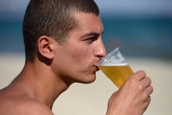 Jovem e bonito homem desportivo bebendo cerveja na praia no verão — Fotografia de Stock