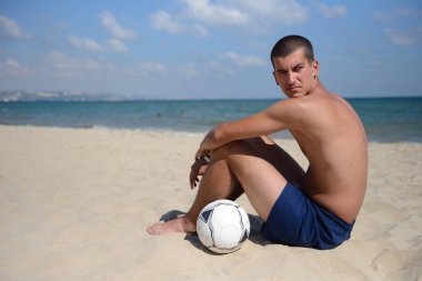 Young man lying on the sand in the with a football ball near him