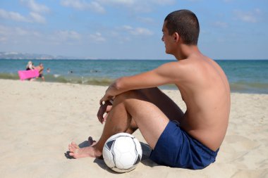 Young man lying on the sand in the with a football ball near him