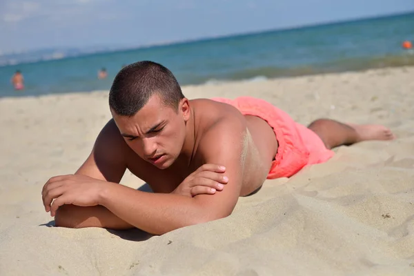 Young man lying on the sand in the sun to tan. Relaxing on vacat — 图库照片