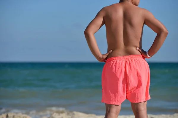 健壮的年轻男人在粉红色短裤坐在沙滩上，看着 — 图库照片