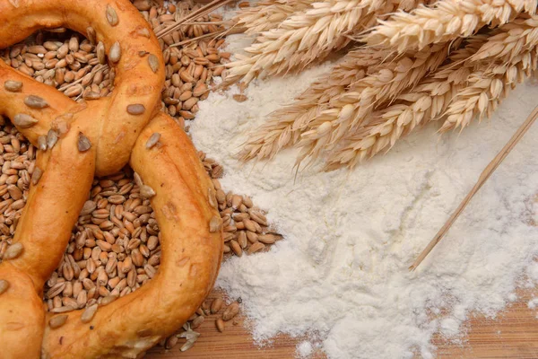 Grains, wheat ears, flour and pretzel on a wooden table. Concept — Stock Photo, Image